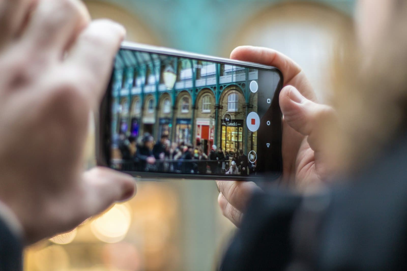 Someone films the inside of a busy covered market on a smartphone held in both hands.
